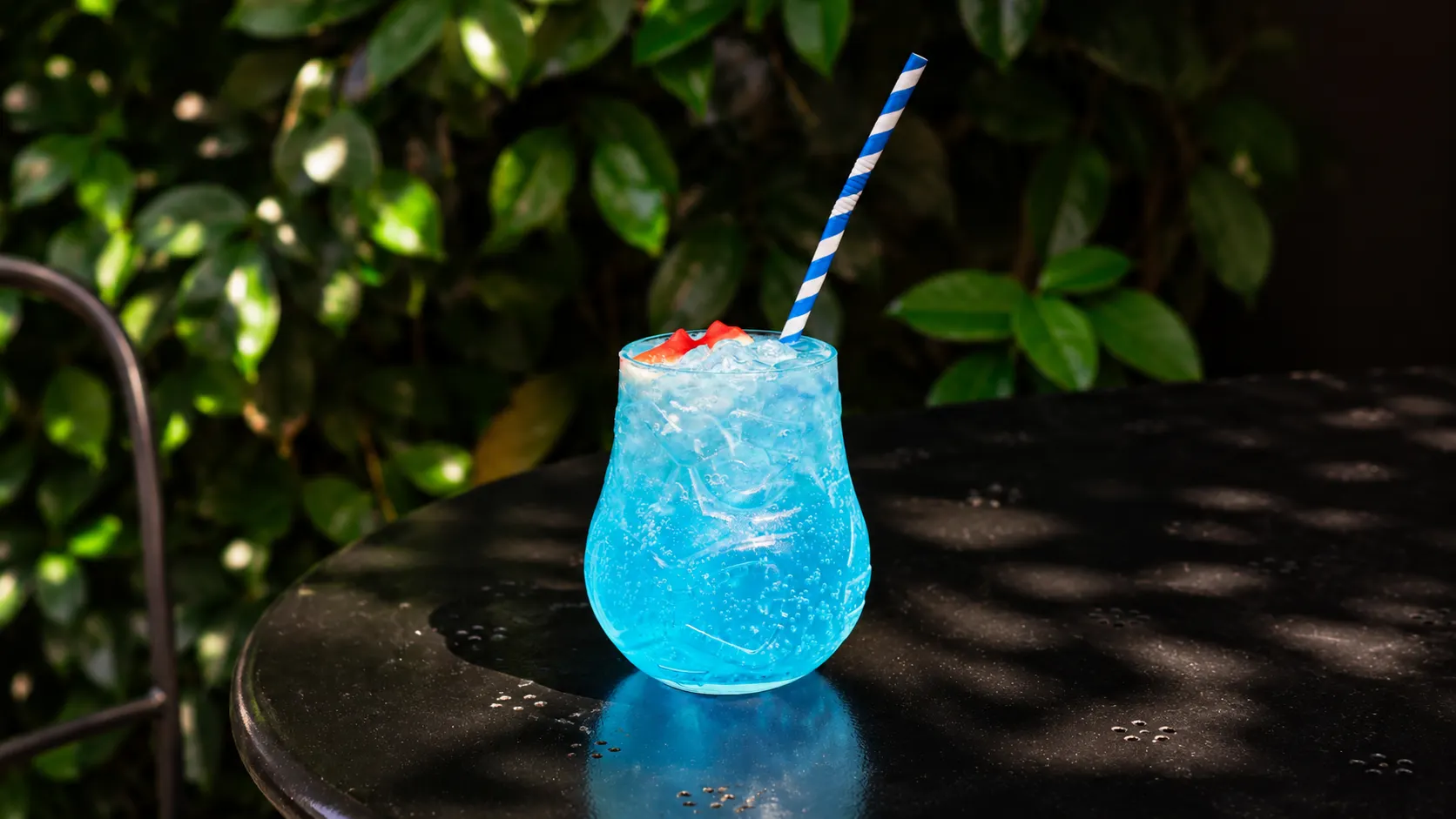 A blue Blue Lagoon in a patterned glass, with crushed ice and a blue-striped straw.
