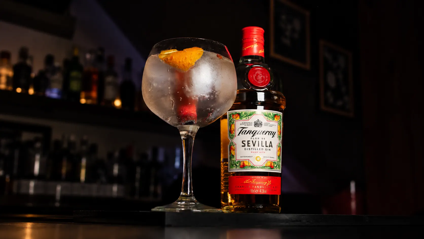 A gin and tonic with orange peel in a balloon glass, beside a bottle of Tanqueray Sevilla.