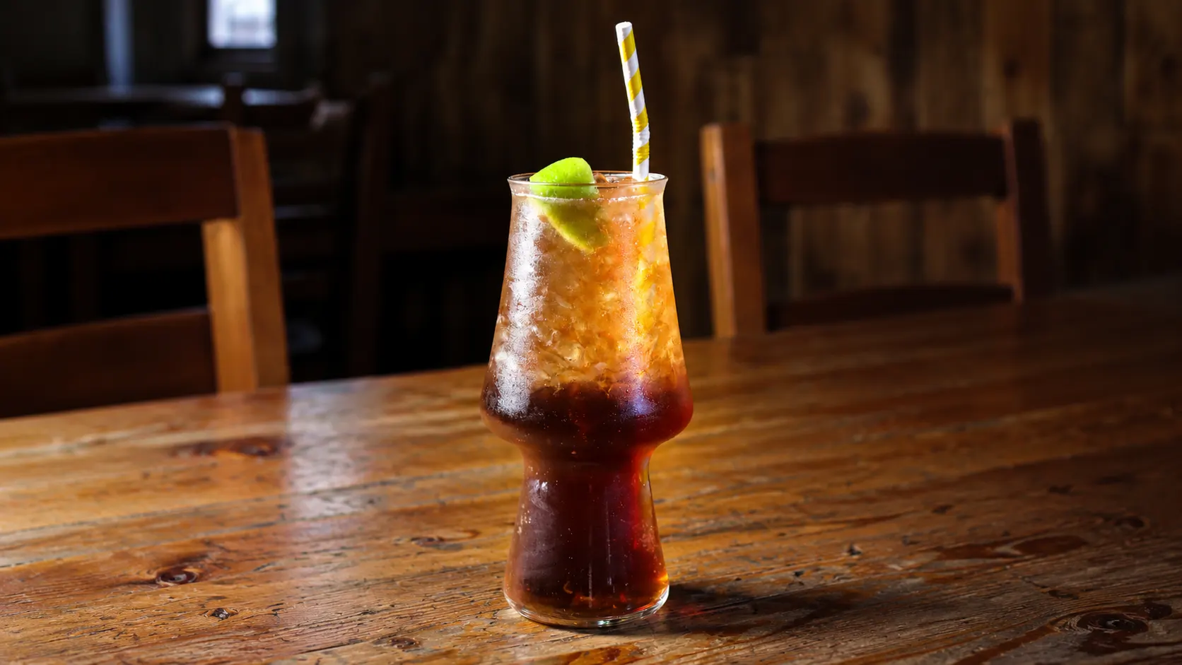 A Long Island Iced Tea in a tall glass, cola-coloured, with ice and a slice of lime.
