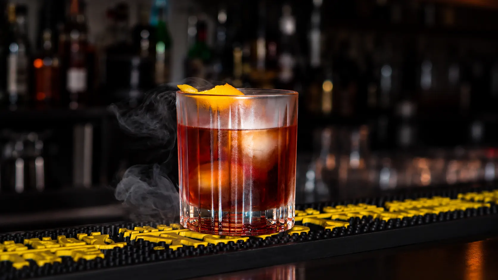A negroni with orange peel, wrapped in smoke, on the bar.