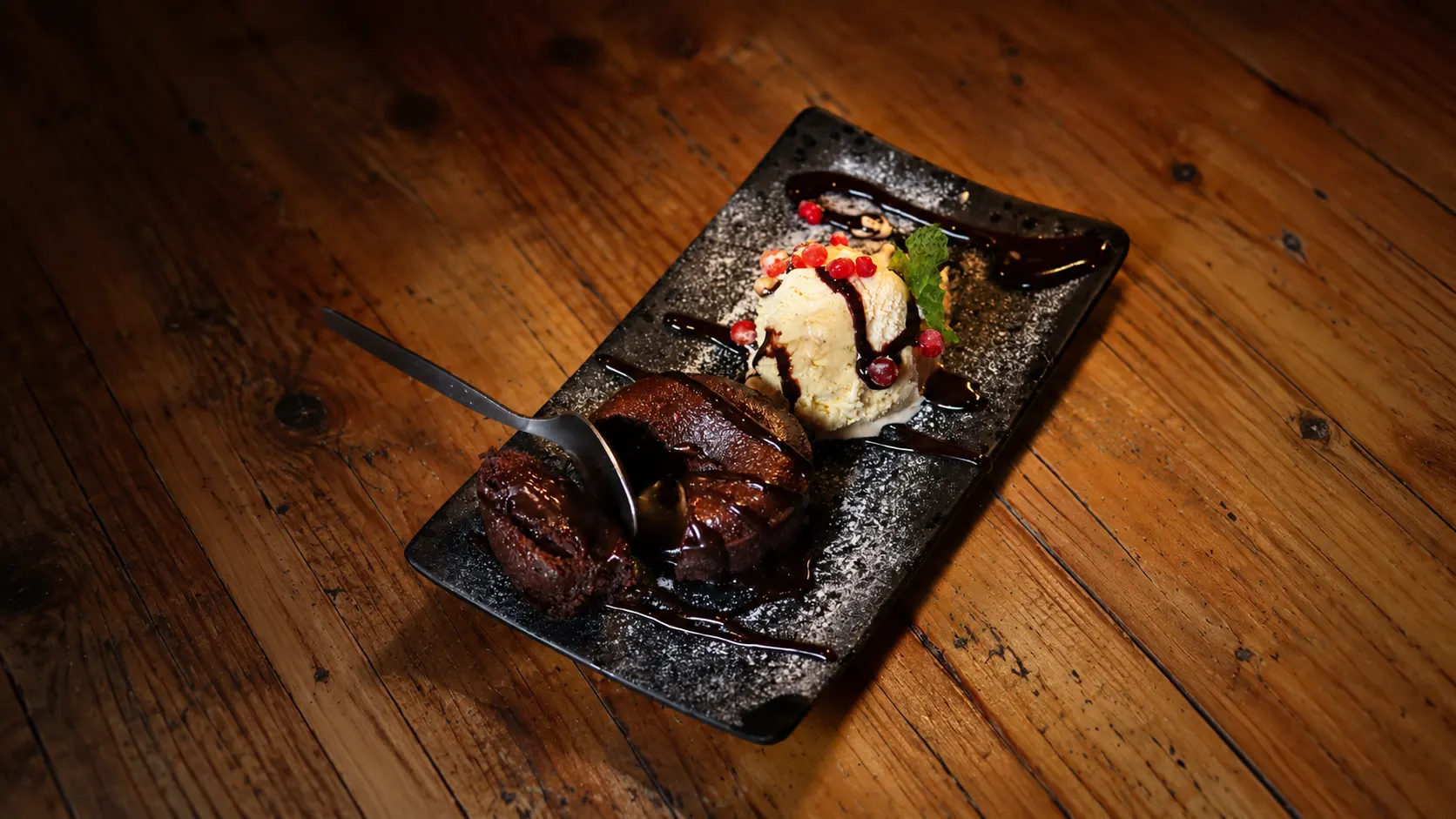 A petit gâteau with a scoop of vanilla ice cream and chocolate drizzle, on a slate plate.