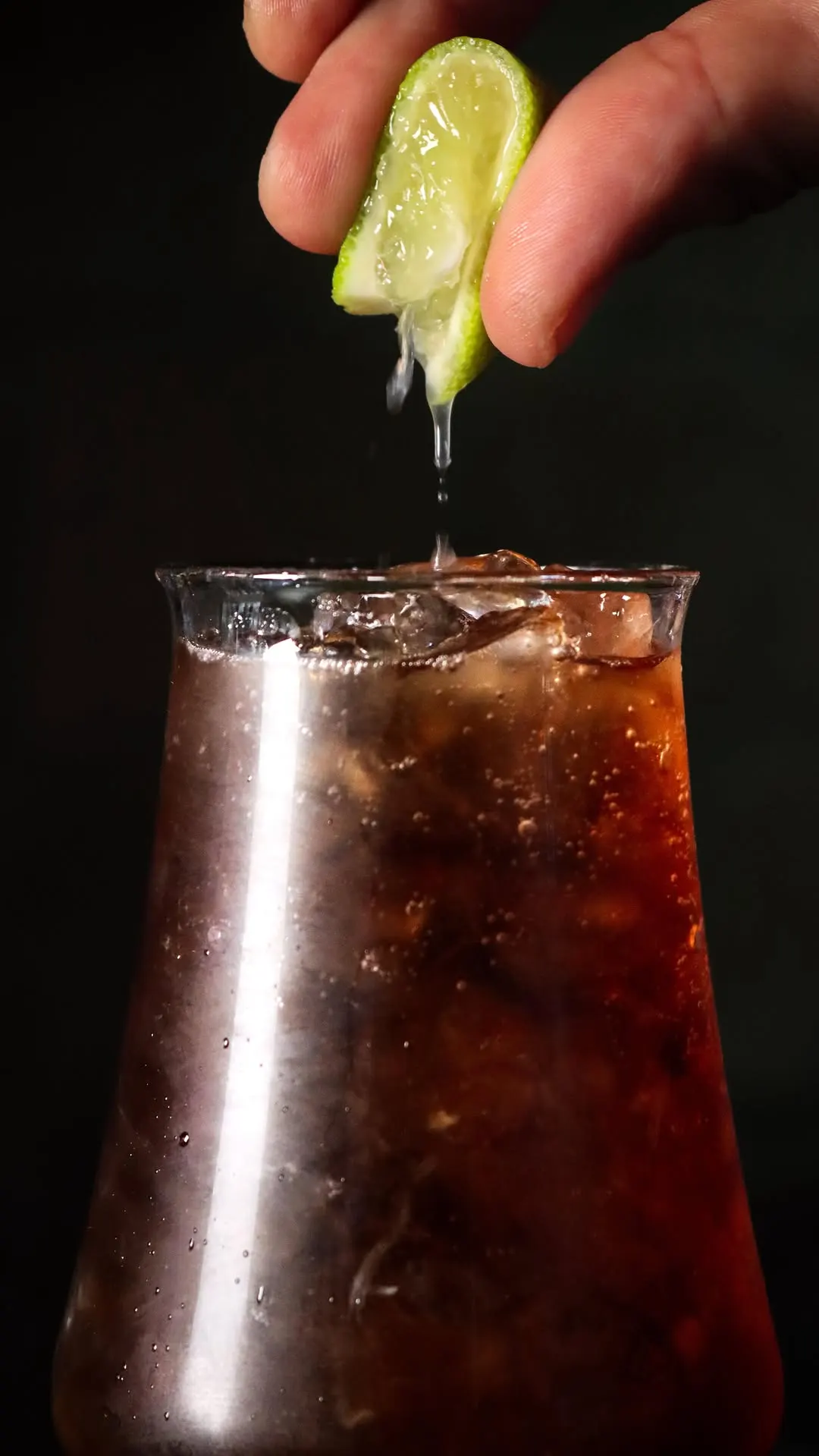 Uma mão a espremer meia lima por cima de um Long Island Iced Tea, num copo alto com gelo.